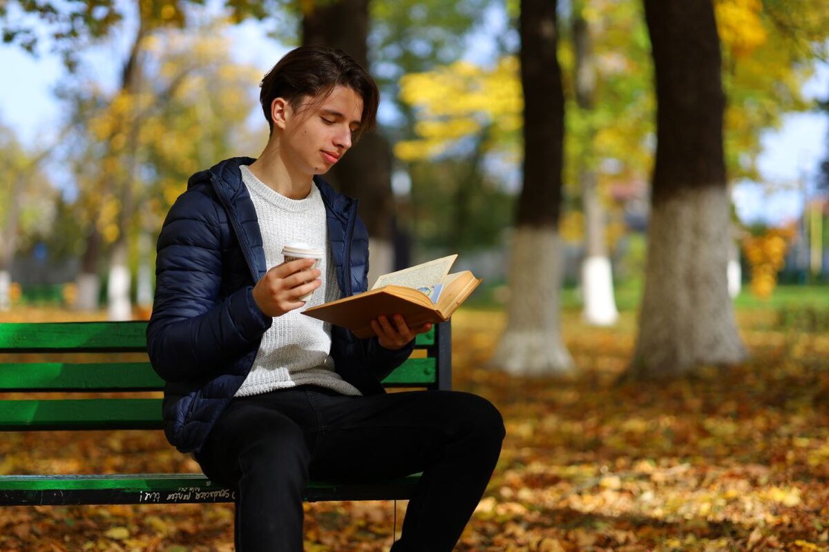 Портрет моего сына, читающего книгу в осеннем парке на скамейке