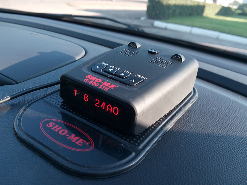 радар-детектор, установленный на нескользящем коврике на приборной панели авто.