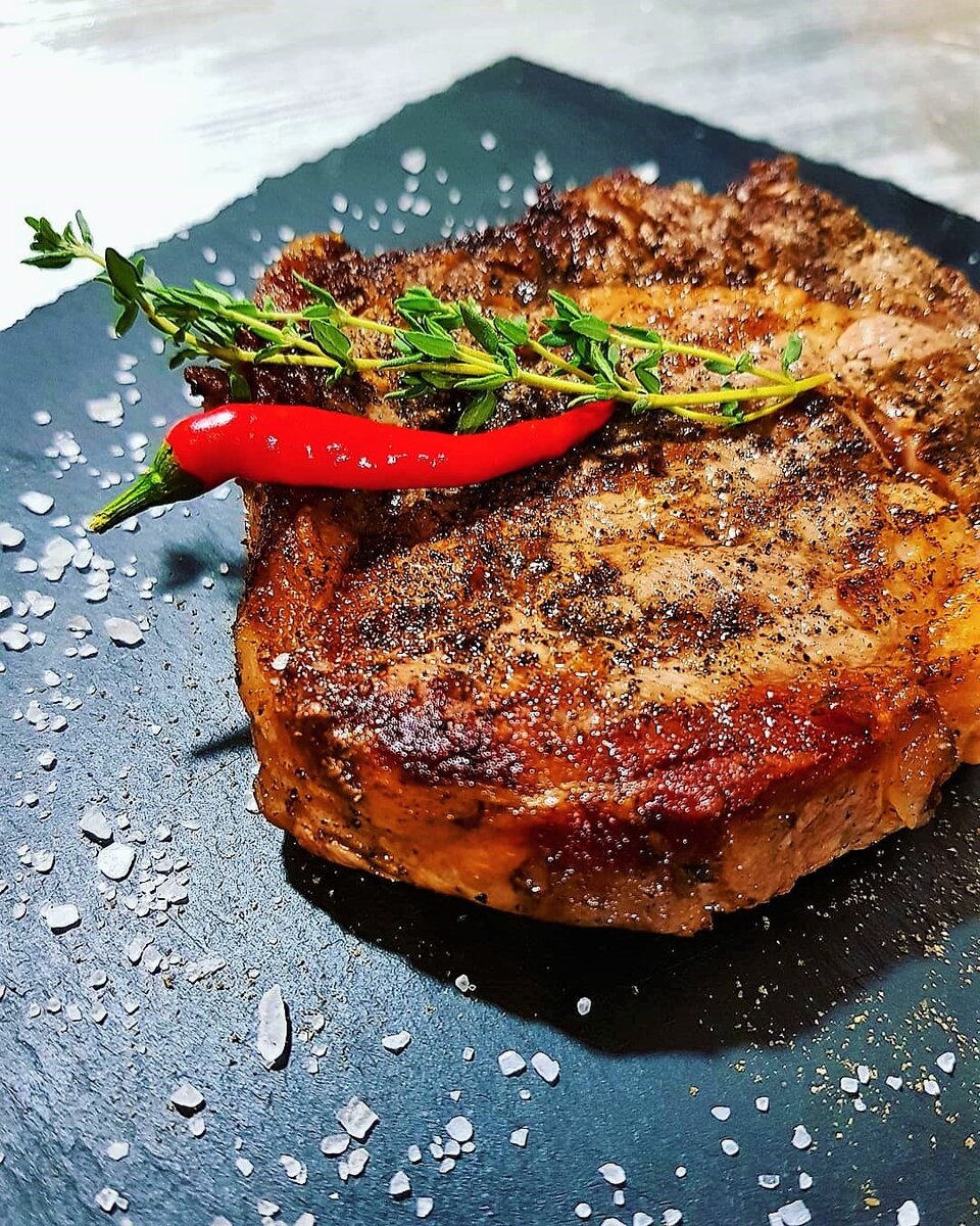 Если вы начинающий повар, то для приготовления стейка лучше использовать толстостенную сковороду (можно готовить на электрическом и угольном гриле, но со сковородой проще соблюдать температурный режим, для определенной степени прожарки). Итак: смазываем стейк с обеих сторон растительным маслом (подойдёт оливковое) и щедро присыпаем солью. Теперь разогреваем сковороду выше среднего (она не должна дымиться, но капнутая на неё капля воды должна собираться в упругий шарик и бегать по сковороде как ошпаренная). 