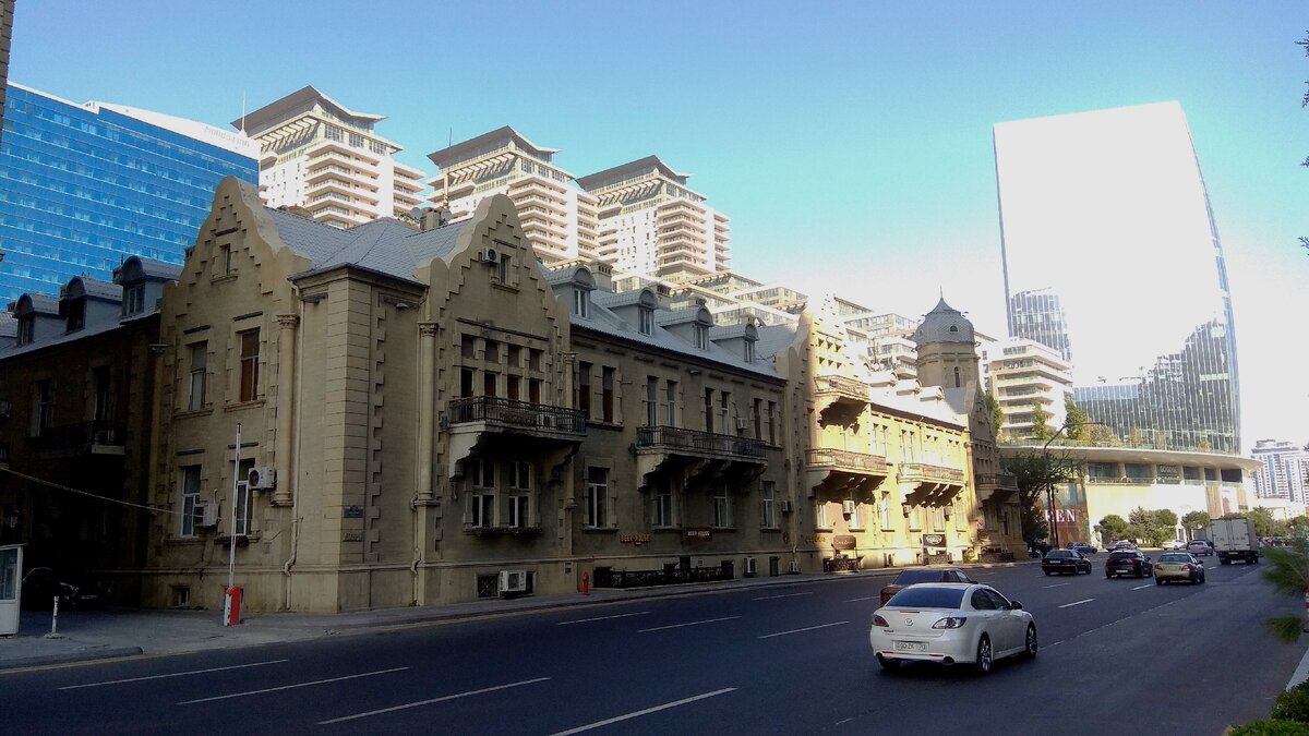 Мы двигаемся по проспекту Нефтяников от центра города. Сочетание разных стилей и эпох. В правой части кадра здание из стекла полностью исчезло в ярком солнце. В галерее три фотографии, которые сделаны последовательно примерно через каждые сто метров.