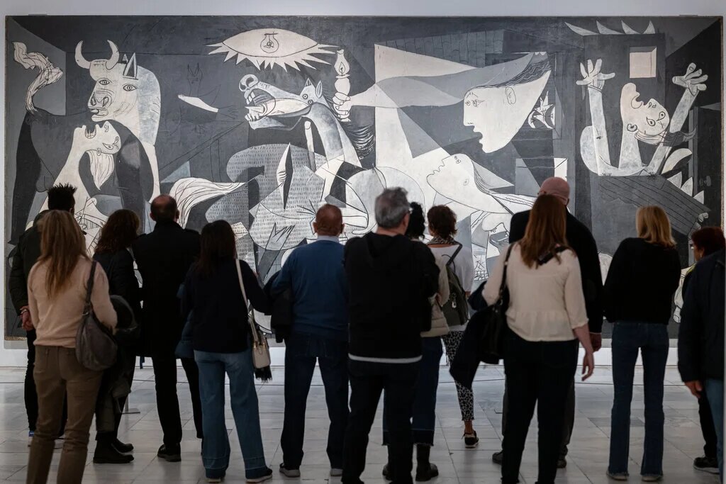 “Герника” Пабло Пикассо (1937), которую рассматривают посетители Музея королевы Софии в Мадриде. Картина является символом ужасных страданий, которые причиняет война.