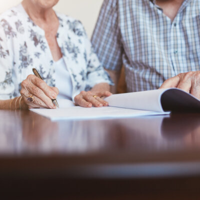    Close up shot of senior woman signing documents with her husband. Elderly caucasian man and woman sitting at home and signing some paperwork, focus on hands. Валерий