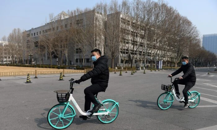 Двое мужчин едут на велосипедах по пустынной территории Университета Цинхуа в Пекине 28 февраля 2020 года. (Greg Baker/AFP via Getty Images)