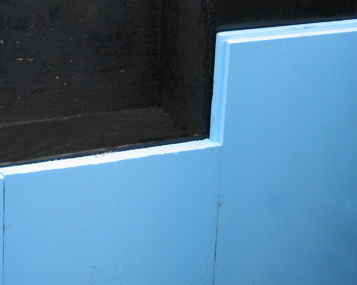 На стены фундамента нанесли обмазочную гидроизоляцию. Затем прикрепили теплоизоляционные плиты из экструдированного пенополистирола. Полимерный утеплитель не намокает (водопоглощение менее 4%) и, по сути, не пропускает воду. 