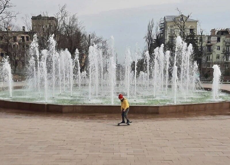 Мариуполь сегодня. Кто-то увидит на фото запущенный фонтан и катающегося на скейте ребёнка. Кто-то, наверняка, обратит внимание на разрушенные здания на заднем плане. Третьи обратят внимание на то, что крышу одного из зданий уже ремонтируют.
