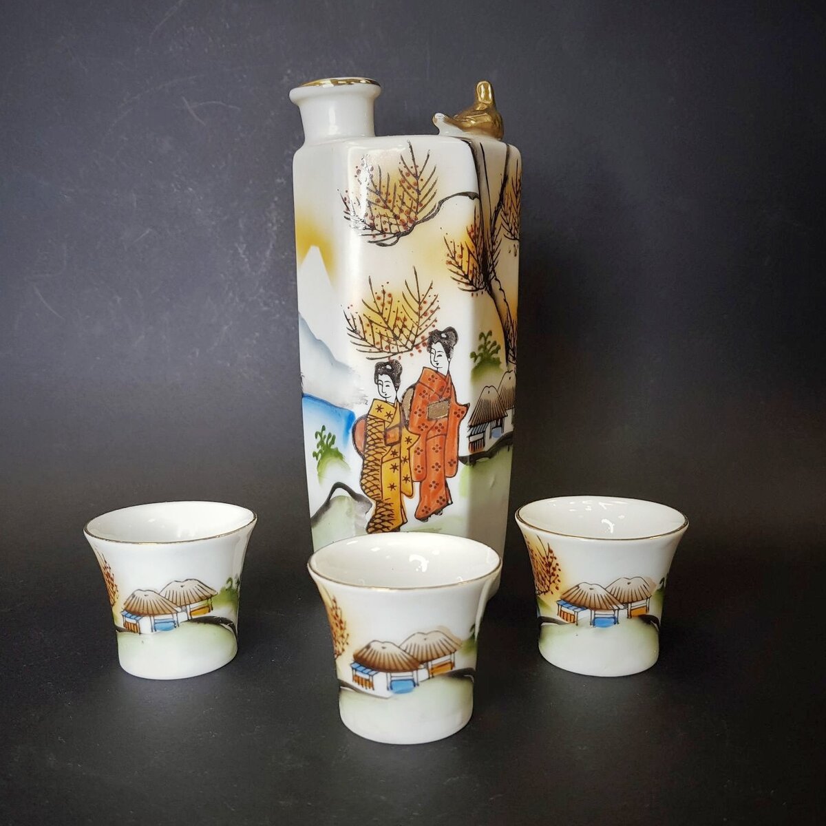 Набор для саке с изображением прогуливающихся гейш и литофанией на донышке стопок. Фарфор, роспись, Япония, 1930-е гг. Высота 14.7 см. https://ru.bidspirit.com