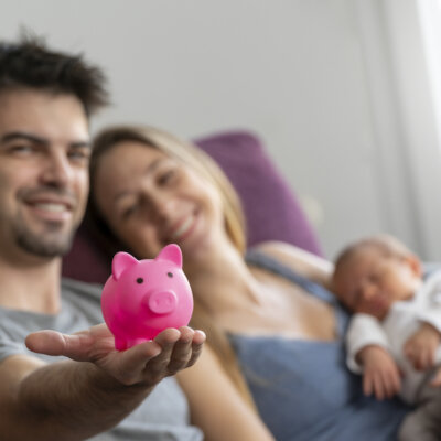    A couple of parents sitting on a sofa in the living room with their baby with a piggy bank Валерий