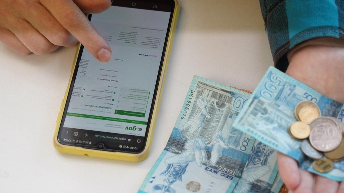    Женщина держит в руках деньги и пользуется смартфоном:NUR.KZ/Владимир Третьяков
