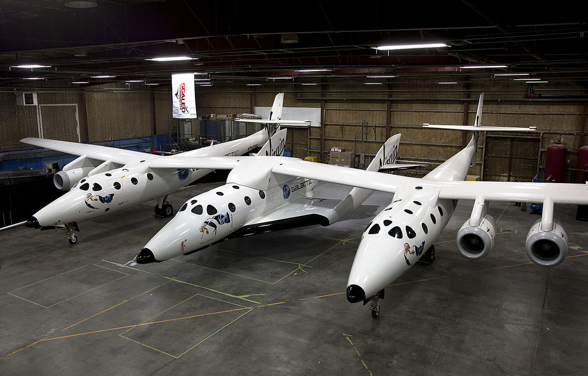 Космический самолет Scaled Composites SpaceShipTwo (центральный фюзеляж) отдыхает под своим базовым кораблем White Knight Two в ангаре в Мохаве, Калифорния, США. Авторство: Virgin Galactic/Mark Greenberg. CC BY-SA 3.0