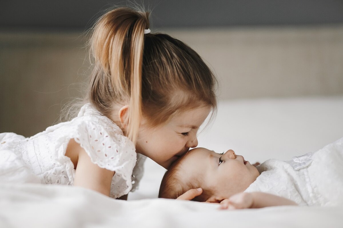    Elder sister is kissing little baby girl in the forehead with closed eyes, kids, maternity, american dream