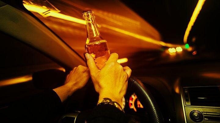    Car driver holds an alcholic beverage while driving at night