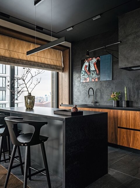 Интерьер кухни формирует чёрный цвет: стены декорированы натуральным сланцем, на полу — крупноформатный керамогранит, салон плитки и сантехники Zodiac Интерьер & Керамика. Лаконичный кухонный остров отделяет кухню от столовой группы. Барные стулья, &Tradition. Кухня с фасадами из ореха, компания VIRS Arch. Яркий акцент интерьера — живописная работа художника Андрея Новикова «Близняшки». Ваза, шар, Keramisu.