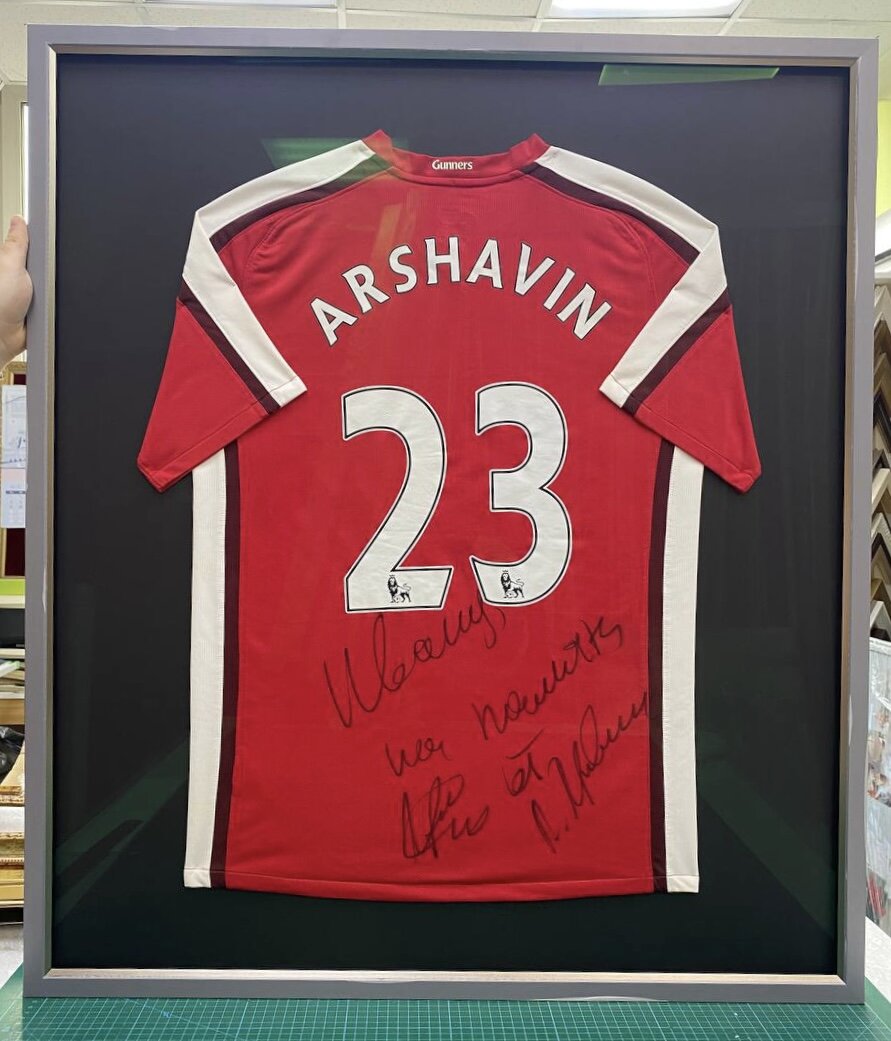 Пример консервационного оформления: футболка с автографом. Материалы: деревянный багет, безбликовое стекло со степенью защиты 70%, консервационное паспарту в качестве основы, консервационный белый задник. Само изделие пришито (не приклеяно!!!), что позволит, при необходимости, достать изделие без повреждения.