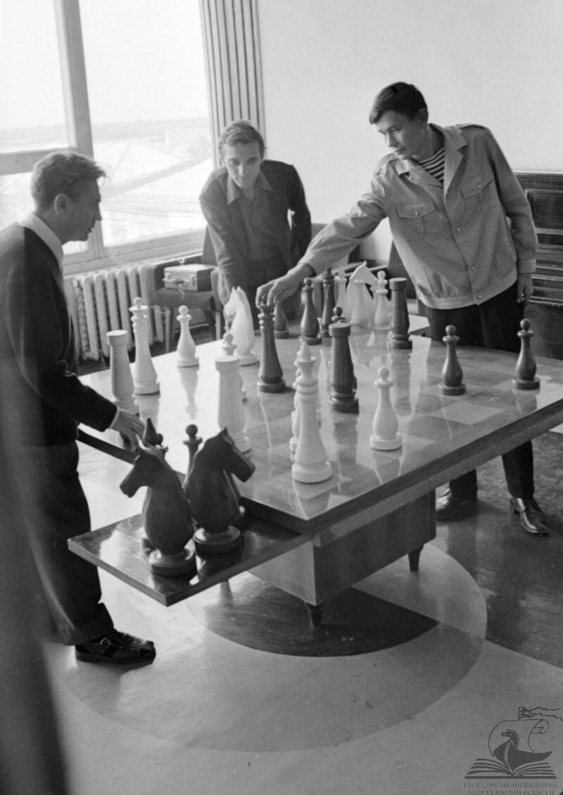 Играют в шахматы: помощник механика теплохода «Адмирал Корнилов» В. Чернов (справа) и инженер А. Бабкин. Наблюдает за игрой инженер-конструктор А. Сластушинский. Астраханский ремонтно-механический завод. 13 октября 1972 г. Фотография Суровцева. ГААО. Нефондовая организация «Фотодокументы». Оп. 22. Д. 22. Л. 1.