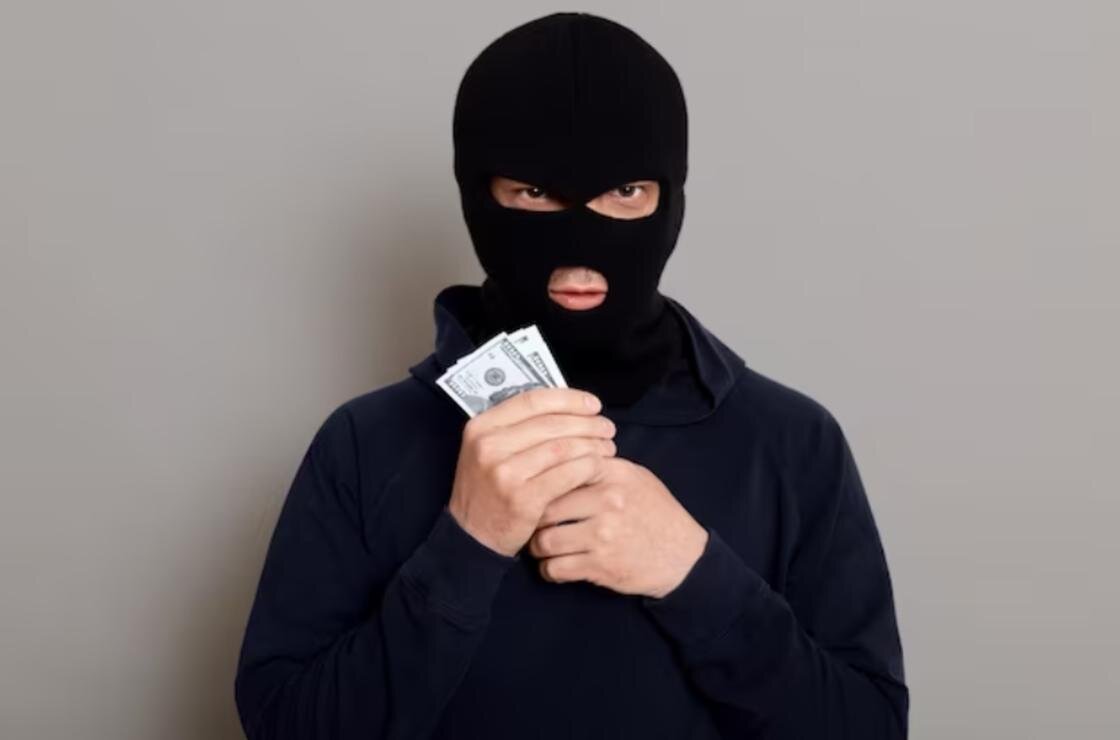    Человек в балаклаве с деньгами в руках:Freepik
