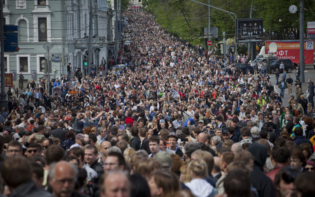 Огромная толпа народа вела по улице. Огромная толпа людей. Скопление людей. Много людей. Толпа людей на улице.