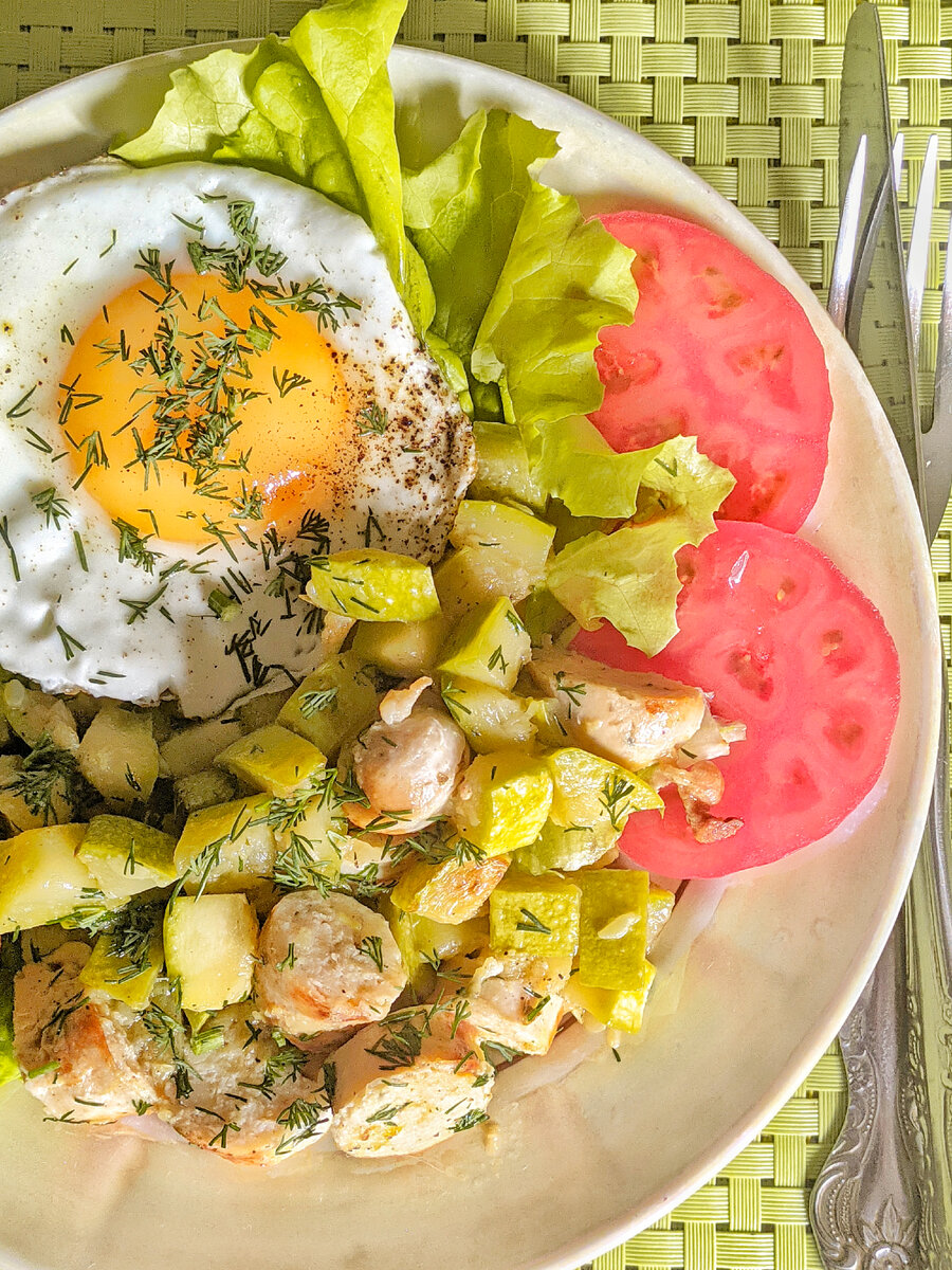 Обжаренные кубики кабачка с куриными колбасками, глазунья, помидор, салатные листья 