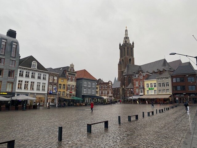 Рурмонд мы осматриваем эпизодически и понемногу, наверное, потому что слишком рчдом живем. В этот  раз мы оказались в центре, на рыночной площади. Рурмонд -  центр нашего региона, он богат старинной архитектурой и культурно развит. Название его означает « устье Рура», а Рур – это река, на которой город расположен. На рыночной площади, прижавшись вплотную друг к другу, буквально в обнимку стоят старые дома, например вот этот серый, в виде пенала. Справа и слева от него находятся худенькие и длинные домики, похожие на чахлые деревца, упорно тянущиеся к свету. Такая узость в облипочку объясняется тем, что стоимость земли под постройки в голландских городах определялась длиной, которое строение занимает вдоль улицы. Но не вглубь, поэтому весь объём построек заключается в вытянутых, как бы втянутых вглубь дворов комнатах, и так в Голландии повсеместно. В центрах  городов в домах редко увидишь квадратные комнаты, они все прямоугольные и сильно вытянуты от уличных окон к противоположным стенам. На выходе из площади стоит католический красавец-собор. Вообще Лимбург - провинция католическая и потому напичкана церквями и соборами. Что мне не нравится  - буквально на каждом углу в городах и деревнях можно увидеть скульптуры и скульптурки распятого на кресте Иисуса Христа. В церкви это уместно. Но тиражировать символ страдания повсеместно как-то странно. В русской ортодоксальной культуре приняты не скульптуры, а иконы. В наших церквях много икон Христа в Силе, с книгой в руке благословляющего паству и икон Божьей Матери с младенцем. У нас Иисус Христос радостный, а здесь он кругом и всюду – переживающий нечеловеческие муки. Идет такое навязывание страдания; кайтесь, посыпайте голову пеплом и бейте себя в грудь. Местные привыкли к этому невеселому антуражу. Они на Христа не смотрят, а идут  в кафе, где весело общаются и пьют пиво.
А вот что в Лимбурге нравится, так это маленькие часовенки имени Божьей матери. Это маленькие строеньца, они могут встертится вам в лесу или на проселочных дорогах. К ним можно подойти, помолиться, поставить свечку пресвятой Марии. Малюсенькую нишу со скульптурой Божьей Матери мы видели в пристройке к рурмондскому дому на узенько улочке, когда шли к парковке.
Немного ниже на этой же улице наше внимание привлекла любопытная фигура: с одной стороны согбенная старушка, с другой – летящая навстречу солнцу молодая красавица. Оказалось, что это памятник персонажу  опере-буф “Schrielhannes” – ведьме по имени Гиацинт. Это опера лимбургского композитора  Йоханеса Юнга, который переработал и использовал в опере известные мелодии из Россини, Моцарта, Брамса и Верди. Опера была написана в 19 веке, и сыграна на лимбургском диалекте в 1860 году, между прочим, уже 160 лет назад. Главный персонаж оперы – немецкий грабитель по имени Йоханес Бюклер, по прозвищу Шхиндерханнес, промышлявший между 1795 и 1802 годом в устье Рейна. Кончил он весьма печально: был пойман с 19 подельниками и гильотинирован. В народных сказаниях он выступает кем-то вроде Робин Гуда, который грабит богатых и делит добычу между бедными. В реальности, однако, все было по-другому: Йохнес был индивидуальным предпринимателем и делился только с членами своей шайки из 2-5 человек.
Опера не имеет отношения к реальной истории грабителя, в либретто он положительный типаж, лимбургский Робин Гуд и ведьма Гиацинт помогает ему установить связь с дьяволом, вероятно, для того чтобы лучше грабить богатых. Всех деталей оперы я пока не знаю, но все заканчивается позитивом. Вот пишу я эти строки и очень захотелось оперу послушать. Ее и сейчас дают в Рурмонде, причем иногда вносят изменения в либретто и придумывают новые арии. Да, надо идти.