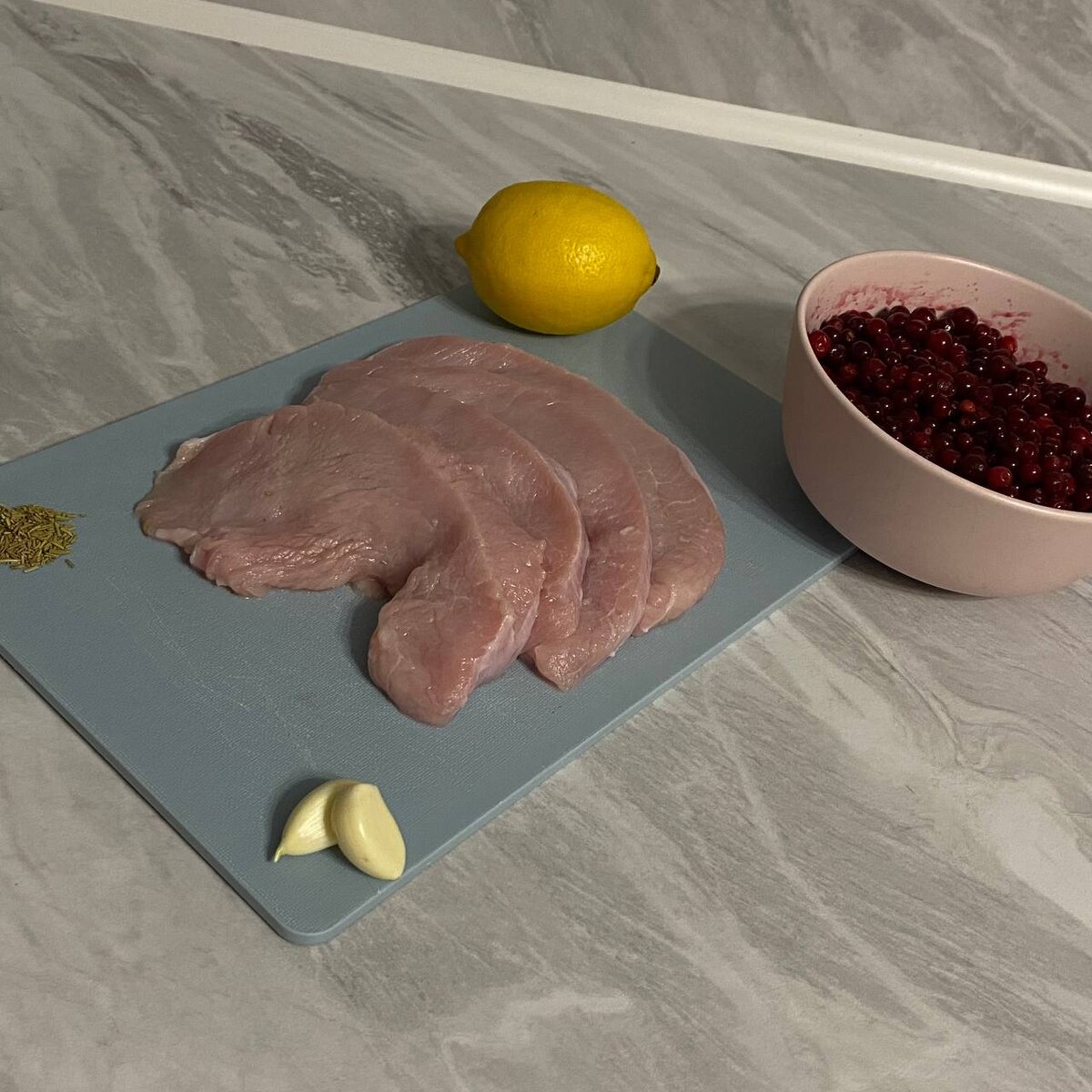 Ингредиенты: •	Стейки индейки – 400 гр.
•	Брусника (замороженная) – 200 гр.
•	Чеснок – 2 зубчика 
•	Масло (сливочное) – 20 гр.
•	Масло (подсолнечное)
•	Соль
•	Сахар – 2 с/л.
•	Перец – щепотку 
•	Розмарин – щепотку 
•	Цедра лимона – щепотку 
•	Вода – 300 мл.
