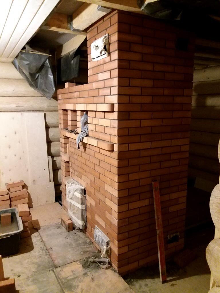 Так это выглядело на первом этаже. Самая большая оклеенная штуковина у пола - дверка в топку. На этой же плоскости у пола и вверху - дверки в кирпичный кожух трубы. Правее от уровня едва видна нижняя дверка вентиляции парной, а верхняя потерялась во мраке. Дверки вентиляции парной находятся на стороне, которая тут не видна.