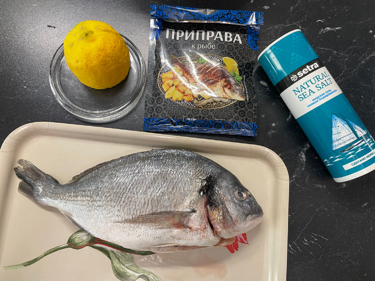 Дорадо почистить, вымыть, высушить бумажным полотенцем. Ножом сделать надрезы по бокам с двух сторон. Посолить, приправить специями, полить лимонным соком. Дольку лимона положить в брюшко. 