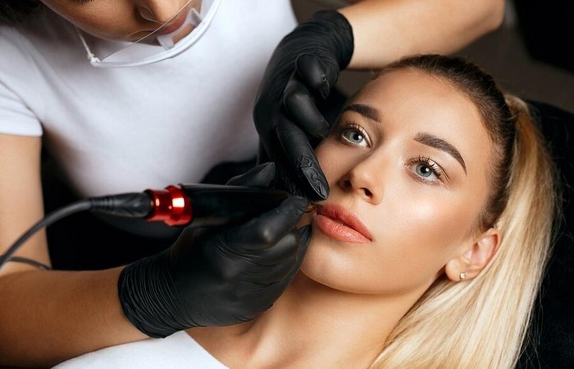    Девушке мастер делает перманентный макияж губ в салоне:Freepik