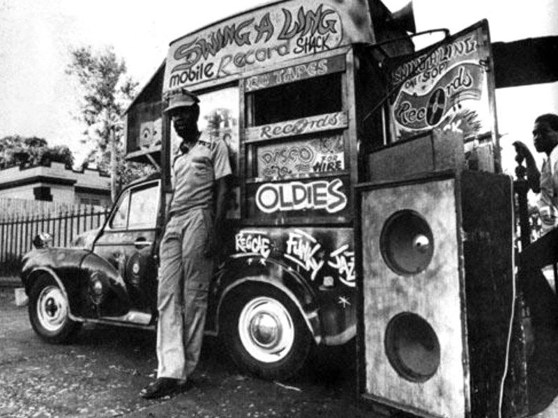 King Tubby рядом со своей мобильной аудиосистемой, звукозаписывающей студией, домом и фургоном с мороженым.