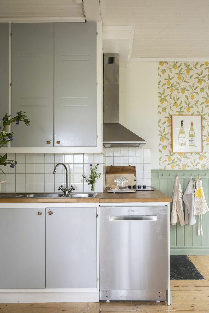 Белый фартук и кухонный гарнитур остались от предыдущих жильцов. В этом интерьере мне нравится то, как обои сочетаются с окружающей обстановкой — деревом, кухонными полотенцами, картиной на стене...