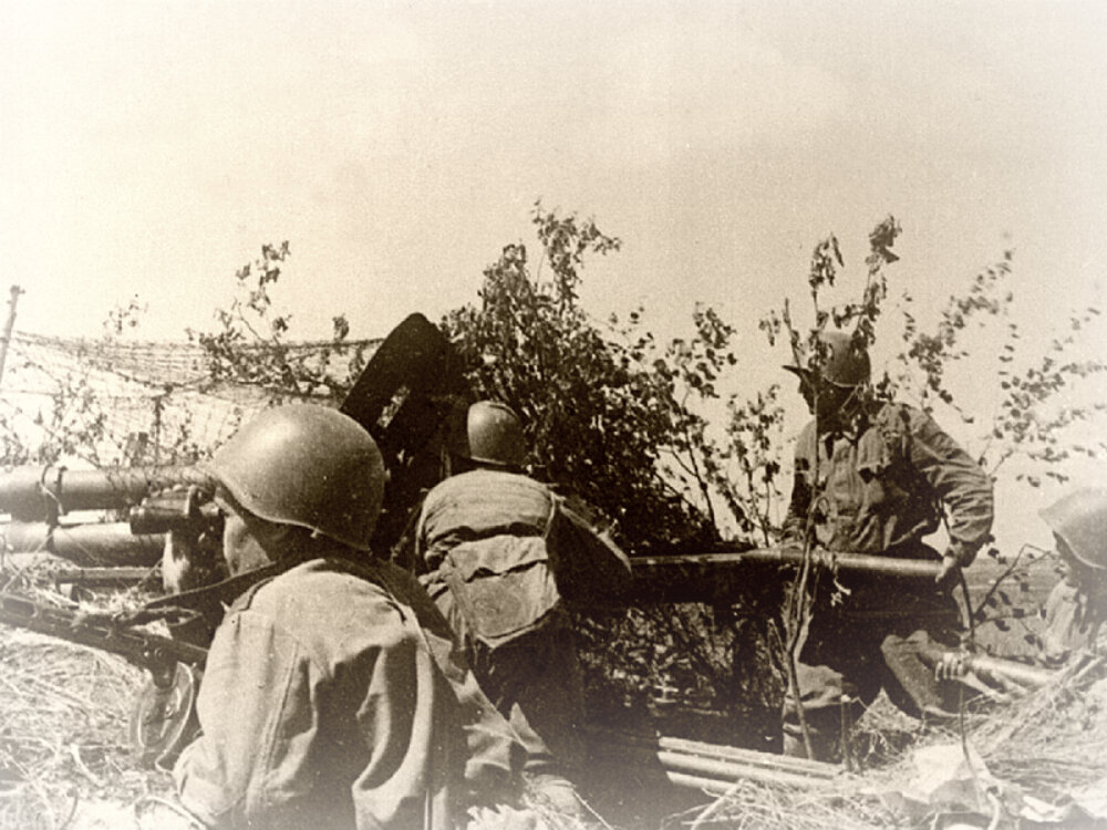Расчет советской 76-мм дивизионной пушки образца 1942 года ЗиС-3 ведет огонь по немецким танкам на Курской дуге. В руках у заряжающего — бронебойный выстрел 53-УБР-354Б со снарядом 53-БР-350Б (трассирующий тупоголовый с баллистическим наконечником с локализаторами). Июнь 1943 г.