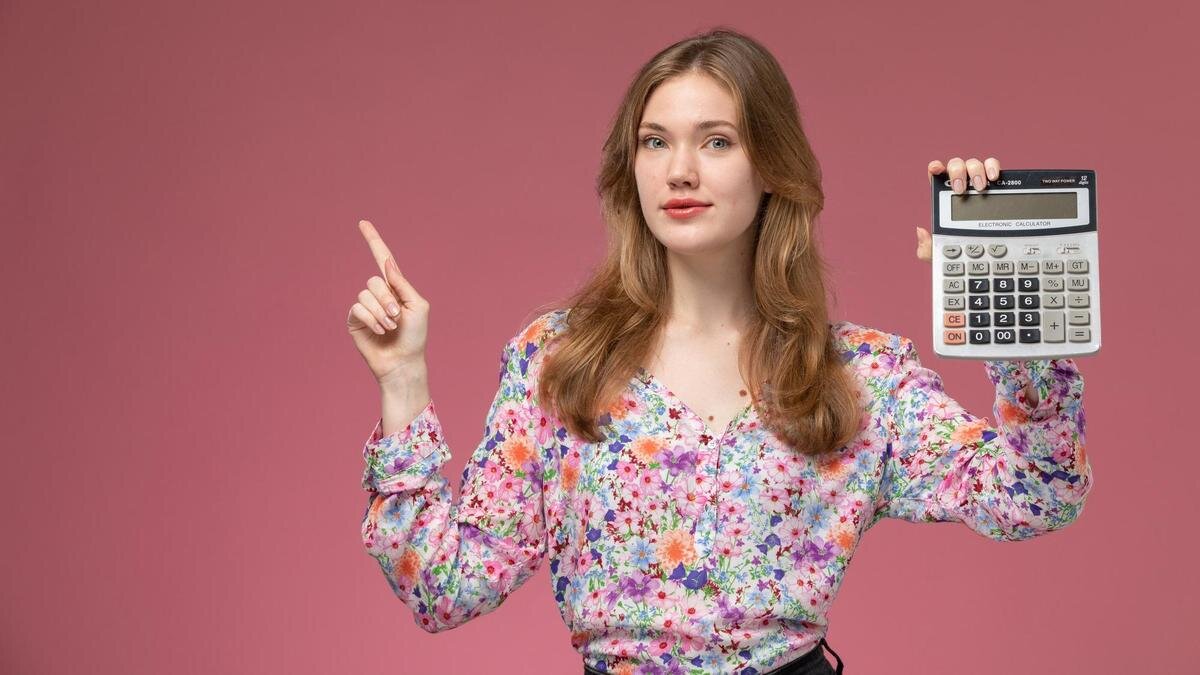    Девушка на розовом фоне держит в руке калькулятор:Freepik/KamranAydinov