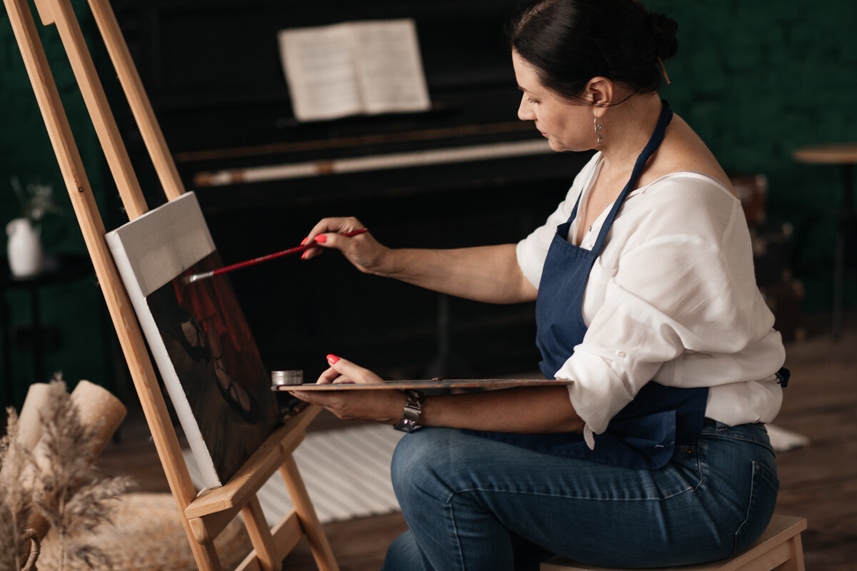 Художник Марго Миро в студии за работой. Художница пишет картину за мольбертом.