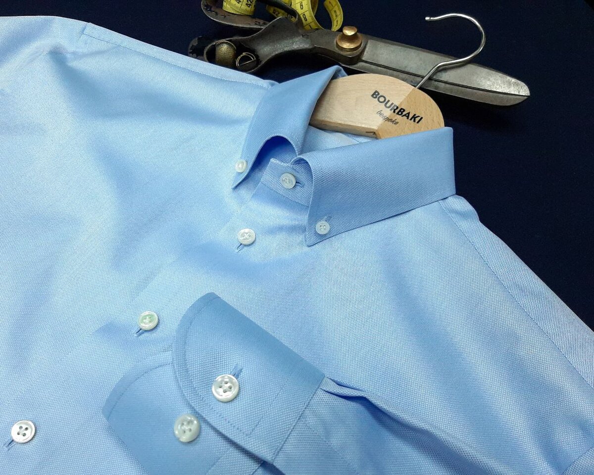 Две похожих сорочки баттен даун с разным характером. Первая из голубого роял-оксфорда Alumo станет прекрасным компаньоном для не слишком формальных костюмов или непарных брюк и пиджаков. Вторая из белого плотного и крупного твила от Caccioppoli подружится с фактурными пиджаками из твида или кардиганами и джинсами. Примечательно, как фактура ткани делает более формальную по цвету белую сорочку менее формальной, чем голубая