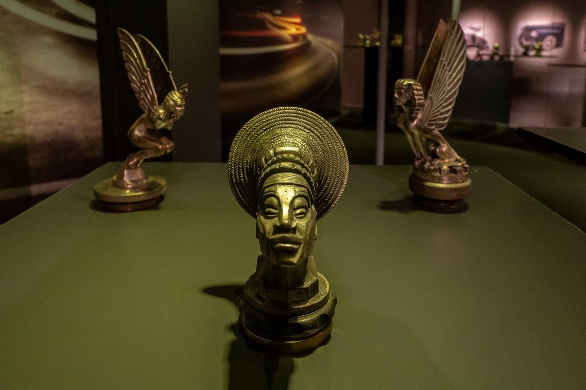 «Африканская принцесса» (на переднем плане) — маскот в стиле ар-деко, созданный Франсуа Базеном. Фигурка изображает правительницу африканского племени Мангбету, которая оказала помощь трансафриканской автомобильной экспедиции 1924–1925 годов. Экспедиция была организована по инициативе Андре Ситроена и проводилась на полугусеничных внедорожниках Citroen B2. (Франция, ок. 1926–1928, алюминиевый сплав, высота — 11 см)

Фото: Олег Золото / MR7