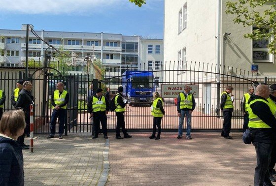    Представители мэрии в сопровождении полиции стоят возле ворот школы при российском посольстве в Варшаве