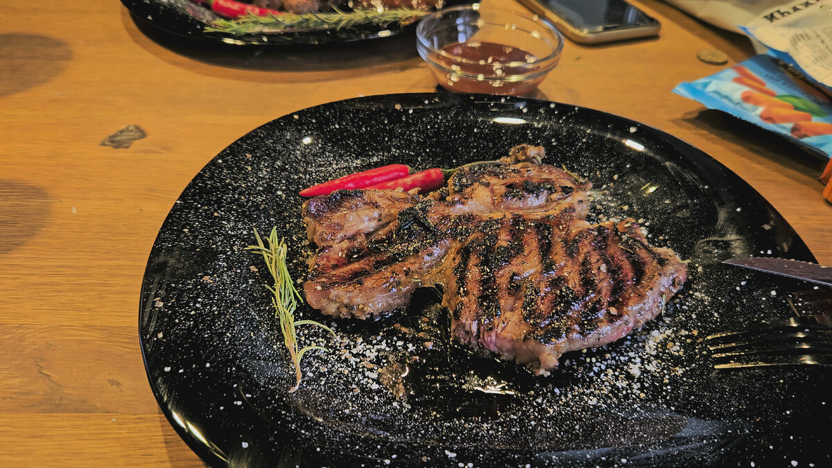 Как приготовить стейк дома вкуснее чем в ресторане. Впервые стейк я попробовал не большом баре в городе, о котором давно уже ходили восторженные слухи друзей и коллег. Все восхищались стейками, и я направился туда из-за любопытства. До этого дня, я достаточно часто слышал о стейках, но в моём понимании это был ну просто жареный кусок мяса. И вот вроде вполне обычный бар, я сажусь и заказываю тот самый стейк и бокал пива, через некаторе время мне принесли мой заказ, передо мной на тарелке в виде лопаты, лежал очень аппетитно выглядевший длинный кусок мяса, я сразу же набросился на него и положив кусок в рот я офигел, это была говядина, но она была такой нежной, такой вкусной и мягкой, до этого я не думал что говядина может быть такой вкусной, я лишь однажды её жарил, перепутав со свининой, она была похожа на подошву от кроссовок, если резалась ножом, то вместе с тарелкой, и если прожевывалась, то вместе с зубами, Позже я зачастил в этот бар, подсел на этот стейк, уже начал расти пивной живот, так же я заказывал стейки и в других ресторанах, но нигде не было такого вкуса, везде был то жесткий, то какой-то варёный, на вкус как кусок мяса на кости из маминого супа, который в детстве обычно обгладывал отец, сидя напротив меня. Просив не малую стоимость за блюдо в этих заведениях, приходило глубокое разочарование из-за отвратительно вкуса. Стейк из неприметного бара задал настолько высокую планку, что я не мог найти нигде чего-то подобного. Да и в один ужасный день я узнал, что такие стейки в этом баре больше не готовят, видно ушёл этот одарённый повар, которого «просто бох в руки поцеловал».
Этот вкус, не давал мне покоя, я пытался воспроизвести что-то подобное, обычно я очень вкусно готовлю, в том числе мясо. Стейки продаются в вакуумах, названий у них столько много, и какие я бы не пробовал, добиться того вкуса и мягкости я не мог, я жарил и на электрогриле и на гриль-сковородке, вся квартира в дыму, результат подошва, уныние. Но я не останавливался, и шёл дальше, стал отбивать стейки молотком, от чего он становился суперслимом 1мм и сгорал за секунду, после чего был похож на птицу, сгоревшую на электропроводах, по которой потом ещё машины ездили. Пробовал разные маринады и так далее, но всё же, я пришёл к тому непревзойдённому вкусу, и сейчас расскажу как:
1. Не нужно покупать слишком тонкие стейки, как «минутка» или «пеппер стейк». Можно найти что-то потолще и не сильно дороге, например «Чак Ролл» или «Стриплойн» ну или пежонский «Рибай»
2. Не надо отбивать молотком, он становится только жёстче, тут подойдёт такой девайс как тендерайзер, такая приспособа с лезвиями, говядина жесткая из-за волокон в структуре, так вот эта штука, своими лезвиями их разрезает, оставляя кусок целым, после такой обработки, стейк становится именно таким нежным, мягким при той же толщине, чем больше раз проткнете, тем мягче будет, в тендерайзерах обычно по 20-30 лезвий.
3. Мариновка. Маринад максимально простой: 2 ст. л соевого соуса, 1 ст. ложку оливкового масла, и чёрный перец, ещё мне понравилось добавлять туда 3 капли «жидкого дыма» придаёт такой вкус, будто приготовили на огне, можно оставить на пару часов чтоб пропитался, а можно сделать инжекцию маринада шприцом во внутрь куска, так будет ещё сочнее, вкуснее и быстрее.
4. Обжарка. Чтобы добиться непревзойдённого вкуса, тут нужен следующий результат: кусок должен быть сырой внутри, а снаружи зажарен полностью, прям сожжен. Для этого нужно выкрутить гриль на максимум, и дать ему разогреться, или на большом огне разогреть гриль-сковороду. Далее, кидаем кусок на гриль и жарим около 2х минут на каждой стороне, на верху стейка должна появиться красная жидкость, это не кровь, не бойтесь!
Если всё сделали именно так, приготовьтесь к тому, что это будет самое вкусное мясо, которое вы ели, как видите ничего сложного, наверно вся загвоздка в подготовке мяса, сейчас технологии уже пошли вперёд, и появились устройства 2в1, и тендерайзер и сразу шприц встроенный с несколькими иглами, позволяет сразу и размягчать и мариновать мясо, что занимает всего пару минут, так же можно мариновать и размягчать шашлык по той же технологии, и удивлять своих друзей и родных своими кулинарными шедеврами!

