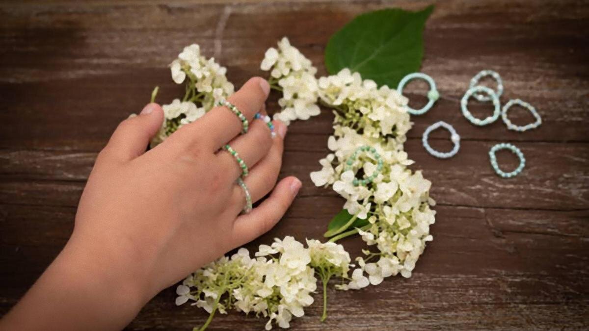    Рука с колечками из бисера на каждом пальце. Рядом на столе лежат белые цветы и колечки:iStockPhoto