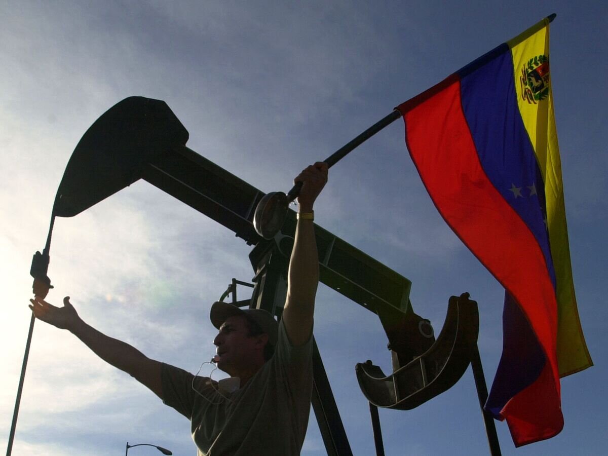    Мужчина с флагом Венесуэлы перед зданием компании PDVSA в Каракасе© AP Photo / Fernando Llano