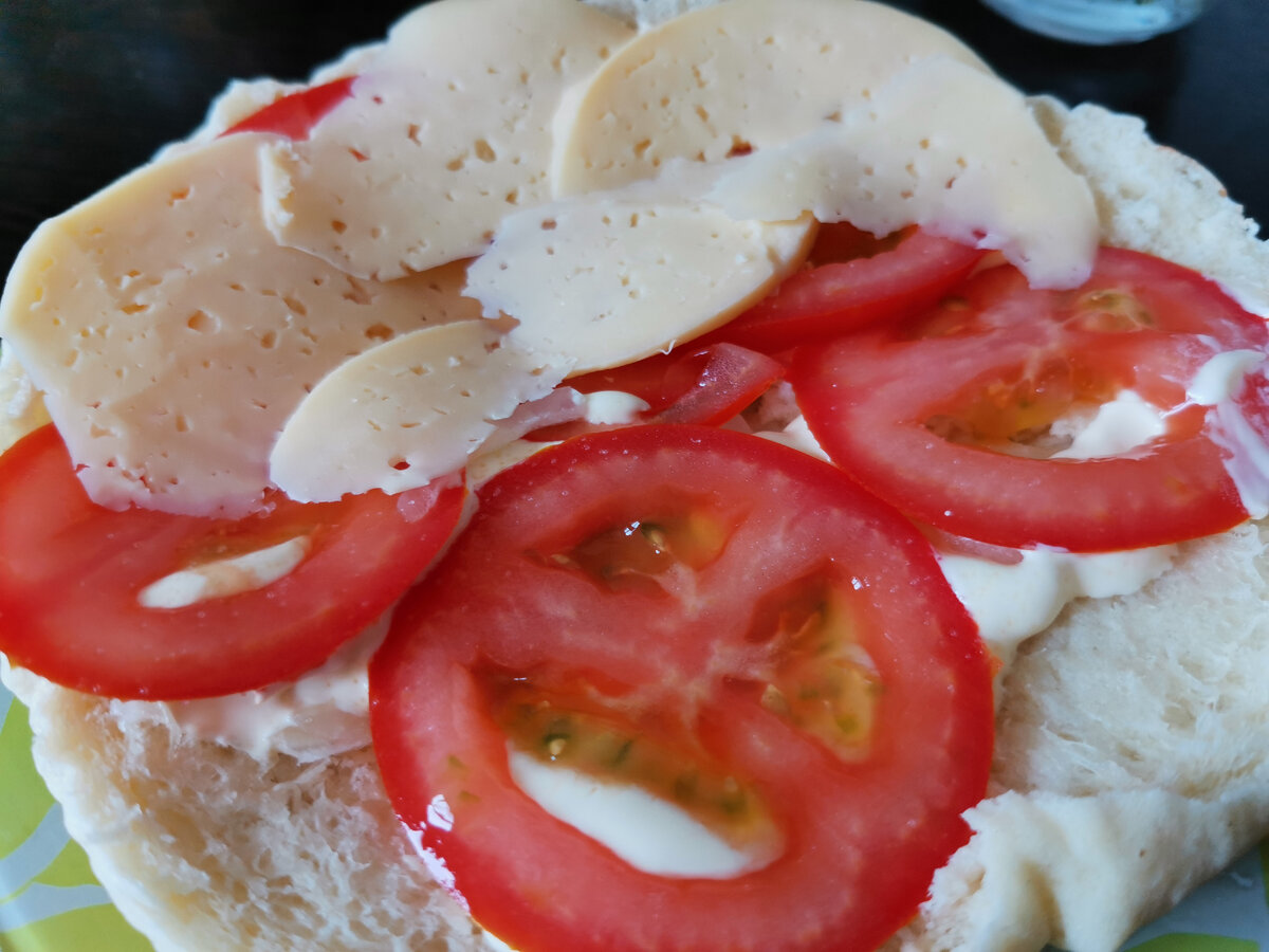 Разрезанная пополам пита с помидорами, луком, майонезом и сыром. 