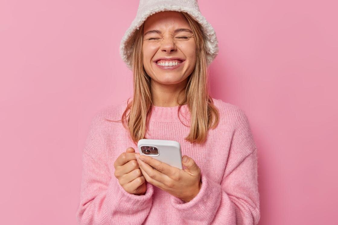    Девушка в панамке держит телефон в руках и смеется:Freepik