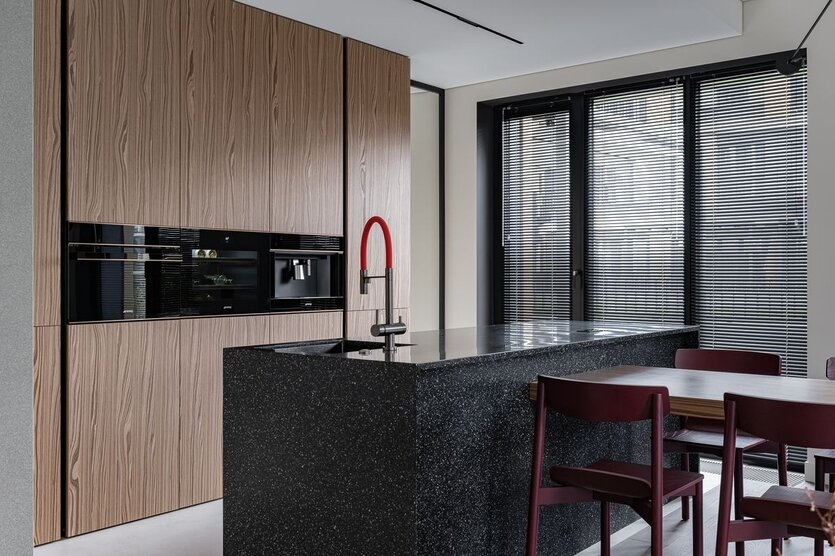 Кухня представляет собой фронт из шкафов со встроенной бытовой техникой. Там расположился встроенный холодильник и секции для хранения. На острове в секции под мойкой установлена система фильтрации воды и диспоузер. Остальные секции — это глубокие выкатные ящики для посуды и кухонной утвари.