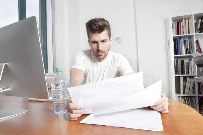 https://focusedcollection.com/ru/180241452/stock-photo-young-man-watching-documents-desk.html