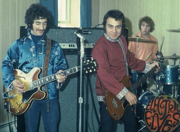 группа под названием The Electric Elves, Ронни посередине (источник фото: https://img.discogs.com/1Bs57qsNezoZgQdmfdrPDjRODG0=/600x441/smart/filters:strip_icc():format(jpeg):mode_rgb():quality(90)/discogs-images/A-2430444-1560055575-1688.jpeg.jpg)