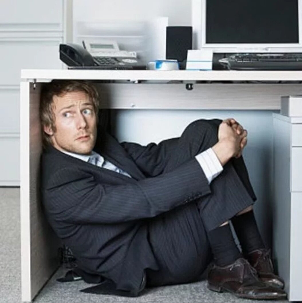 Нестандартный сотрудник. Человек прячется. Офисный работник. Человек под столом офис. Человек прячется под столом.