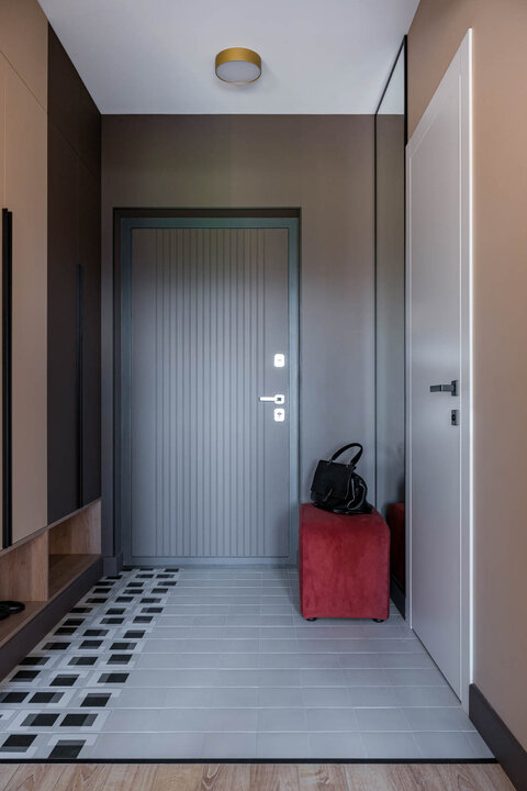 Прихожая. Пол выложен керамогранитом 41zero42 с рисунком, напоминающим ковёр. Пуф выполнен по эскизам дизайнеров мастерской «Rubini». Межкомнатная дверь, компания «Волховец». Шкаф изготовлен на заказ по эскизам дизайнеров в студии мебели «ВарАлекс».