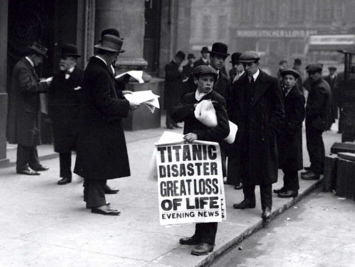 Мальчик газетчик, держит большой постер. На нём огромными буквами написано: «Гибель Титаника! Большое количество жертв!»