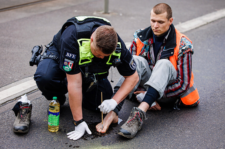 Полицейский в Берлине пытается отклеить от асфальта ногу активиста из «Последнего поколения». Фото: EPA/CLEMENS BILAN