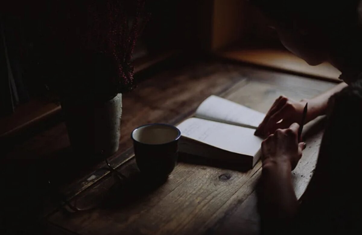 Темная комната книга. Чтение в одиночестве. Чтение на ночь. Женская рука на столе. Человек за столом в полумраке.