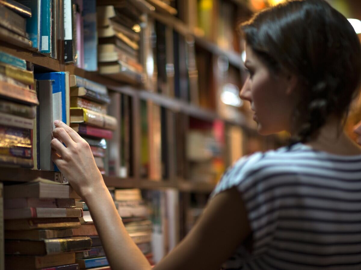    Девушка выбирает книгу в библиотеке© iStock.com / 4FR