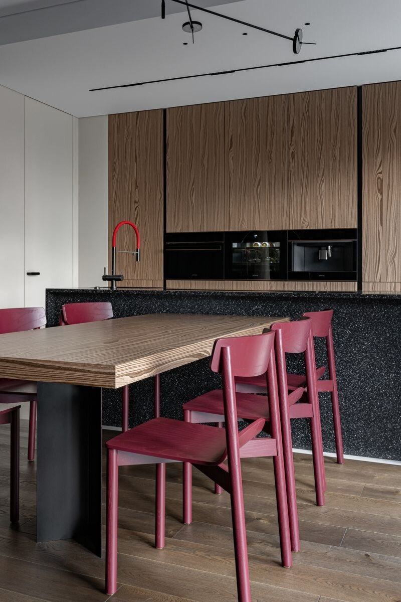 Стулья Artu из массива ясеня окрашены производителем в винный цвет по заказу дизайнеров. Это, по сути, единственное, помимо смесителя, цветовое пятно в сдержанной палитре интерьера. Подвесной светильник Grok добавляет графики. Бытовая техника, Smeg.