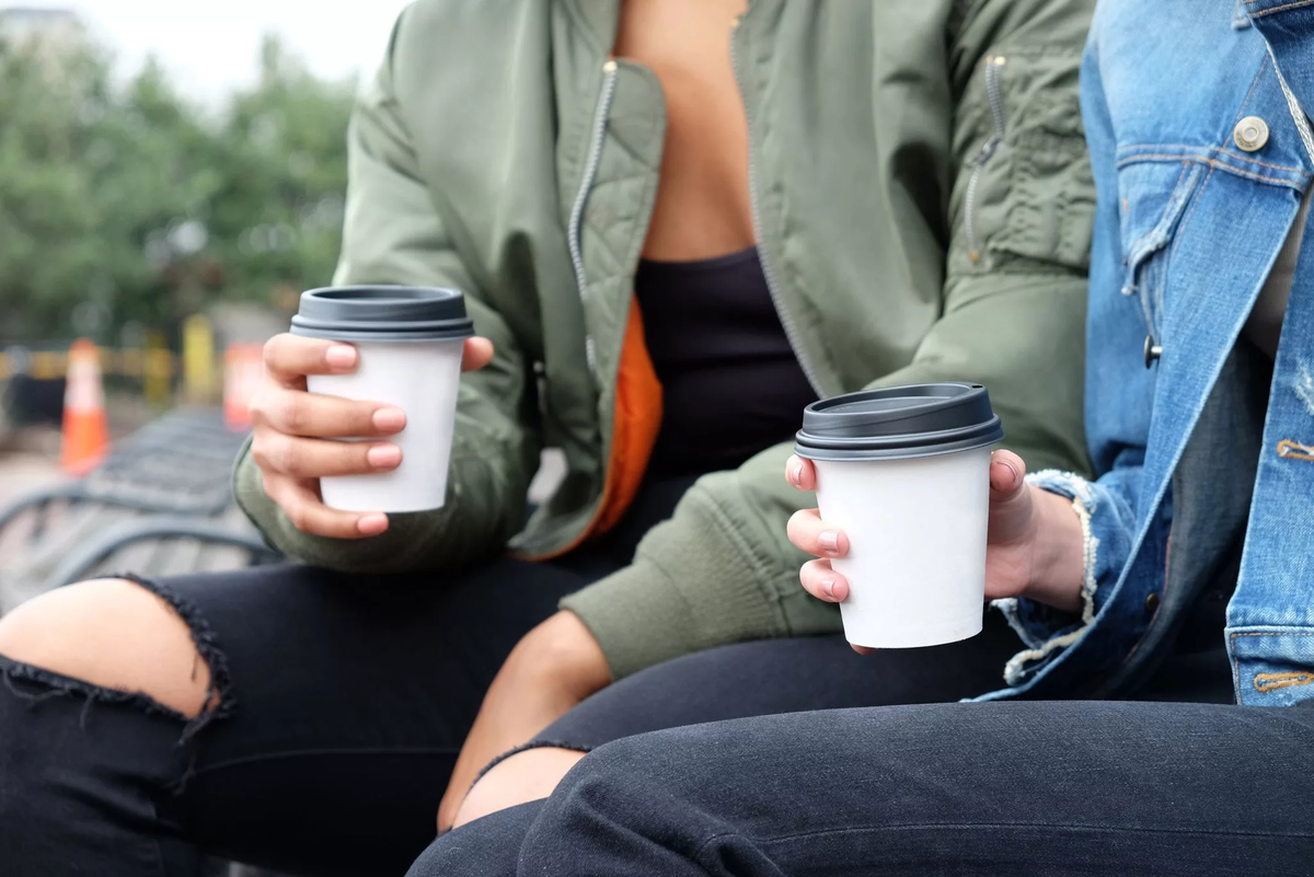 девушка пьет кофе на улице. ход человека. быстрая еда на ходу. человек со стаканом кофе на улице. перекус на бегу.